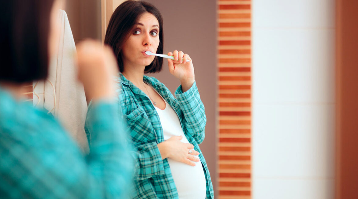 Pregnant woman brushing her teeth in front of a mirror