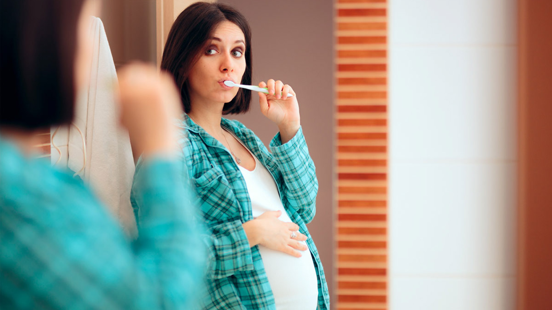 Pregnant woman brushing her teeth in front of a mirror