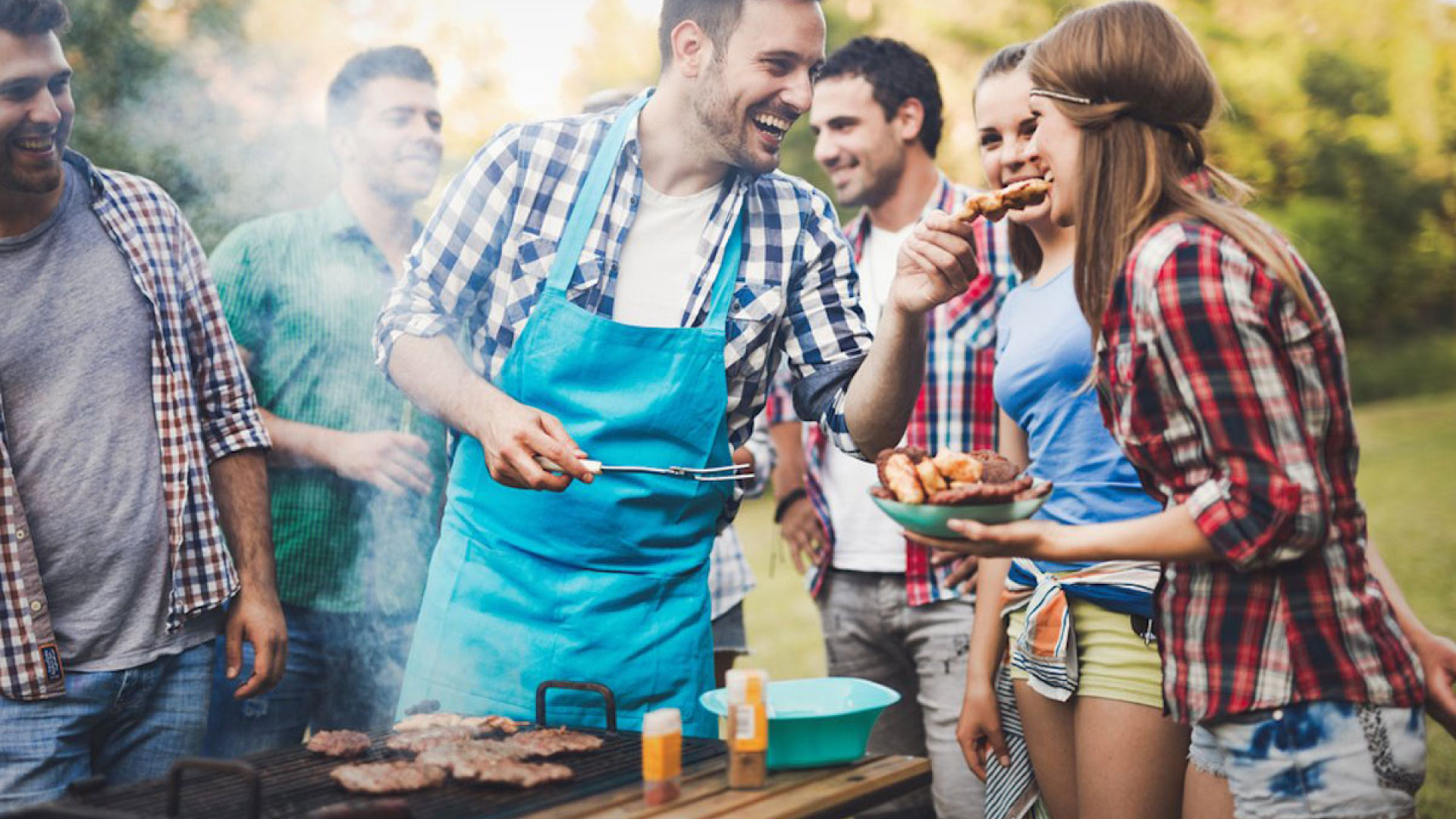 A group of happy people enjoying a summer barbecue, grilling a variety of foods, for Dr. Lenia’s Dental Surgery blog article titled ‘Summer Barbecue: How to Enjoy Grills Without Damaging Teeth