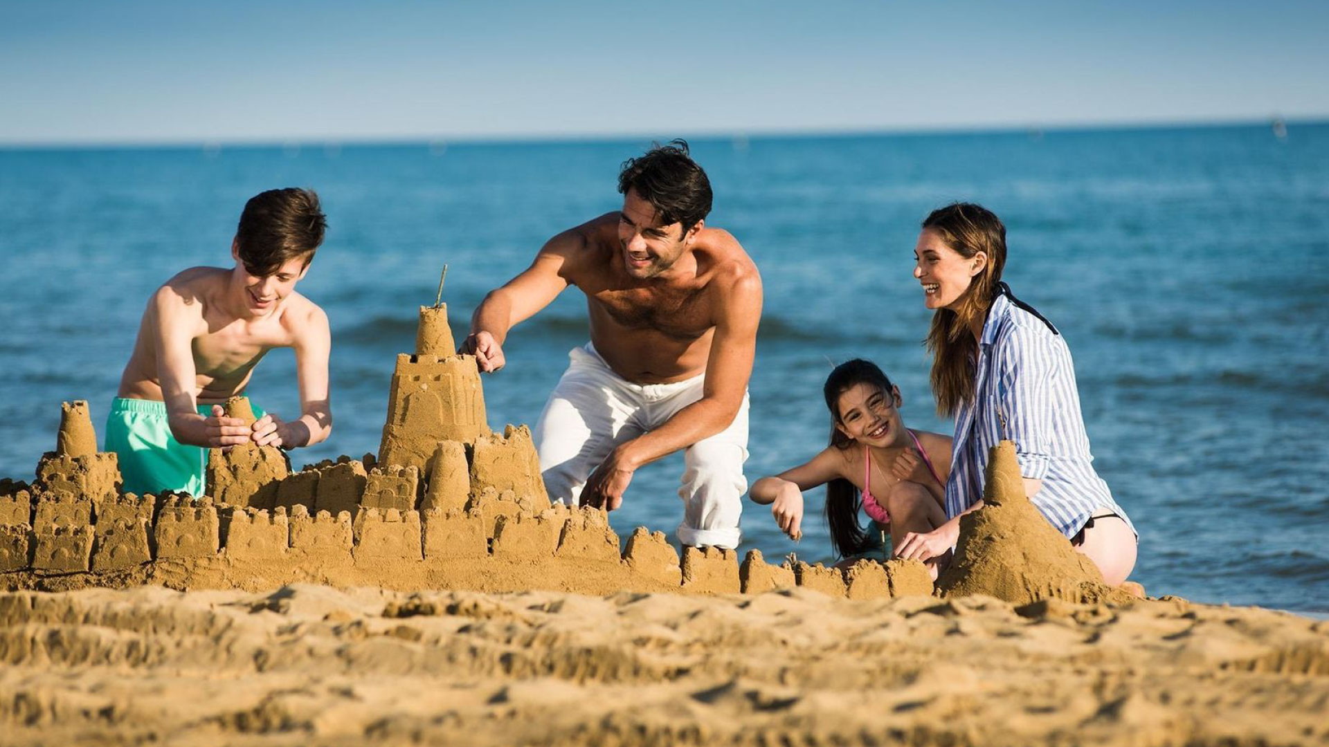 A happy family with children building sandcastles on the beach, all smiling and enjoying a day by the sea. Oral hygiene at the beach.