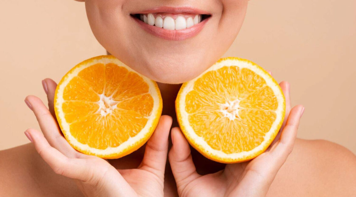 Smiling woman holding orange halves, showcasing vitamins for healthy gums. Discover the best vitamins for healthy gums at Dr. Lenia’s Dental Surgery.