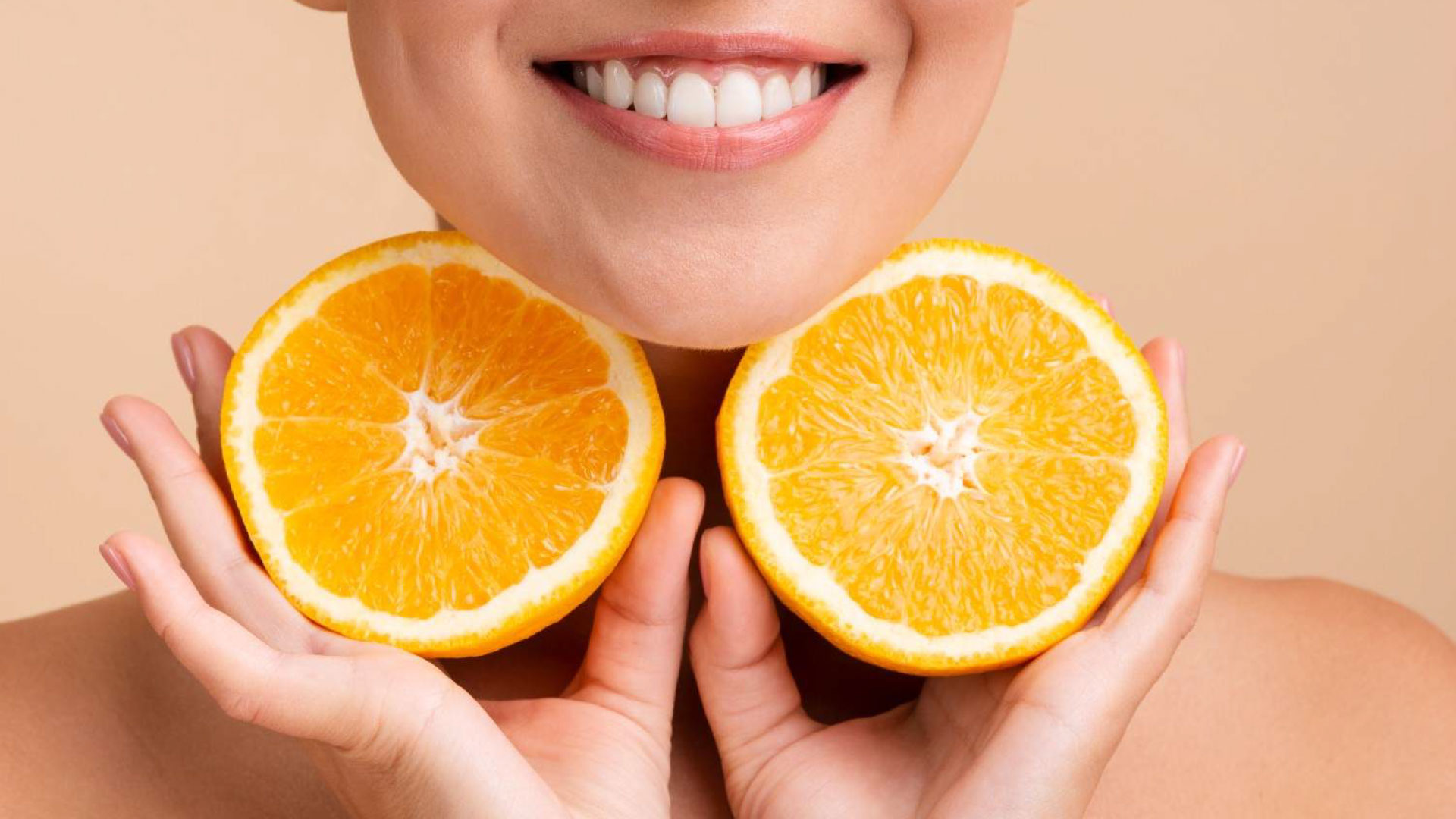 Smiling woman holding orange halves, showcasing vitamins for healthy gums. Discover the best vitamins for healthy gums at Dr. Lenia’s Dental Surgery.