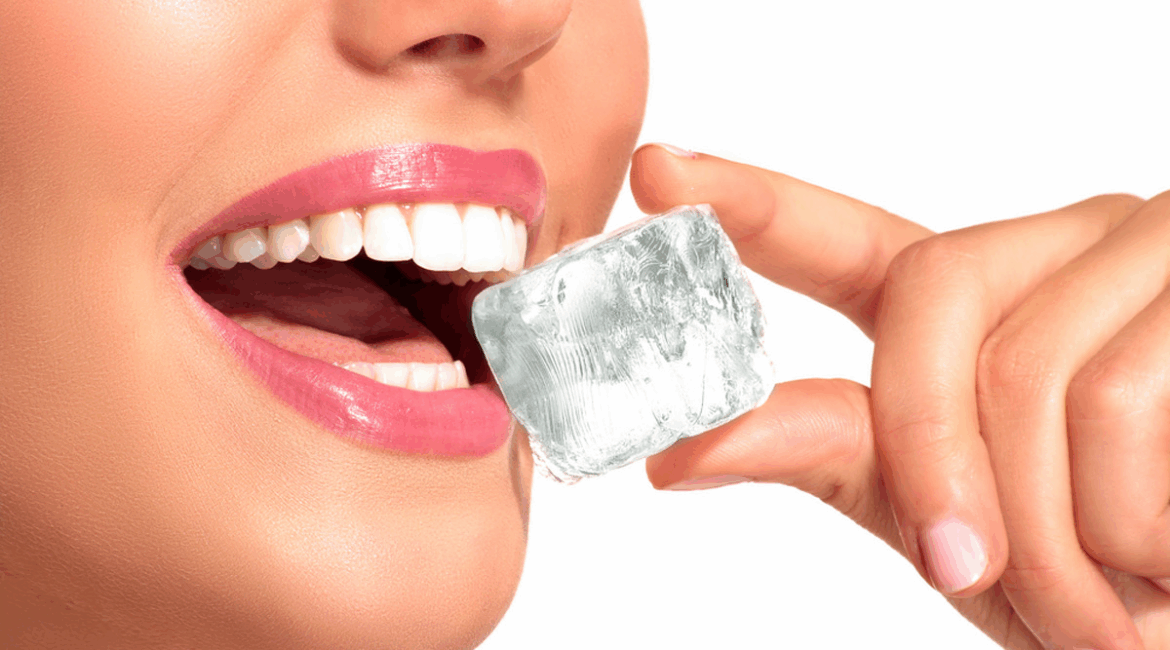 A gentle hand holds a transparent ice cube as a bright smile with perfectly white teeth reaches to grab it. The image symbolizes the contrast between freshness and dental sensitivity, highlighting the issue of sensitive teeth summer caused by cold and summer environmental triggers.